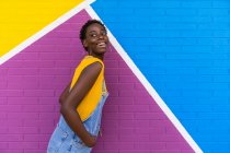 Side view of happy young African American female smiling while standing on colorful bright wall — Stock Photo