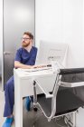 Hombre con uniforme médico escribiendo en el teclado de la computadora mientras trabaja en la clínica de salud - foto de stock