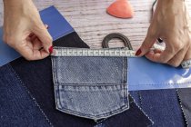 High angle of crop anonymous female dressmaker measuring jeans pocket on wooden table in daytime — Stock Photo