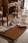 White tablecloth and plates placed on festive table decorated with burning candles and dry branches of tree — Stock Photo
