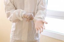 Crop anonymous male medic in PPE suit putting on latex gloves while preparing for work during coronavirus pandemic in hospital — Stock Photo