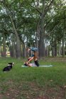 Вид сбоку гибкой пары, которая в дневное время вместе занимается акройогой на коврике для йоги на траве против деревьев в парке — стоковое фото