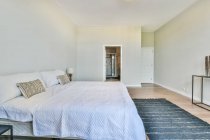 Moderne spacieuse chambre en costume intérieur meublé avec un lit confortable avec table de chevet près de tapis et salle de bains — Photo de stock