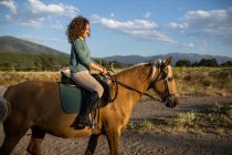 Side view of female riding stallion with smooth brown coat on rough land against mount in countryside — Stock Photo