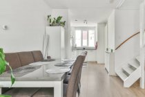 Пустой обеденный стол и стулья размещены в светлой комнате с белой мебелью в современной квартире в дневное время — стоковое фото