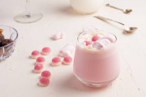 Glass of sweet hot white chocolate with pink jelly candies and marshmallow served on white table — Stock Photo