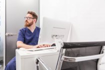 Чоловік в медичній формі друку на клавіатурі комп'ютера під час роботи в клініці охорони здоров'я — стокове фото