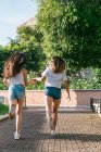 Back view of anonymous best female friends holding hands while running on tiled walkway in town — Stock Photo