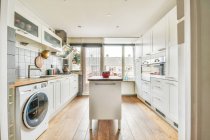 Интерьер просторной кухни с современной бытовой техникой и белой мебелью в квартире оформлен в минимальном стиле — стоковое фото