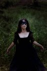 From above mystic witch in long black dress and with painted face standing looking up in dark gloomy woods — Stock Photo