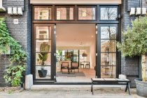 Patio mit Bank und Pflanzen gegen zeitgenössisches Wohnhaus mit Ziegelwänden und offenen Türen am Tag — Stockfoto