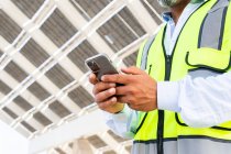 Foreman irriconoscibile ritagliato in panciotto navigando sullo smartphone mentre in piedi vicino alla centrale solare — Foto stock
