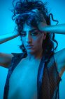 Jovem transexual modelo masculino com maquiagem na jaqueta elegante olhando para a câmera no fundo azul — Fotografia de Stock