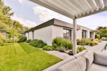 Prato erboso verde e piante tropicali nel cortile della casa moderna con accogliente zona salotto con comodi divani nella giornata di sole — Foto stock