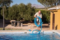 Corpo completo di uomo anziano in occhiali da vista in piedi con tubo di gomma per piscina — Foto stock