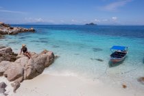 Reisenden mit Hut sitzt auf Steinen am sandigen Ufer des klaren türkisfarbenen Meeres in Malaysia — Stockfoto