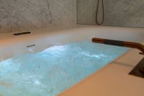 Interior do banheiro contemporâneo com banheira de hidromassagem com água limpa contra parede de luz no apartamento — Fotografia de Stock