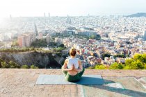 Desde arriba vista trasera de una mujer anónima flexible con las manos orantes detrás de la espalda practicando yoga en la alfombra en la ciudad soleada - foto de stock