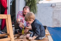 Unshaven pai maduro com menino atento medindo blocos de madeira com fita enquanto passa o tempo em fundo borrado — Fotografia de Stock