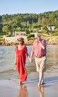 Sourire pieds nus couple âgé dans des lunettes de soleil debout sur la plage de sable humide et profiter d'une journée ensoleillée — Photo de stock