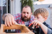 Unshaven pai maduro com menino atento medindo blocos de madeira com fita enquanto passa o tempo em fundo borrado — Fotografia de Stock