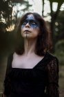 Містична відьма в довгій чорній сукні і з пофарбованим обличчям, що стоїть в темному похмурому лісі — стокове фото