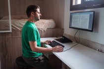 Vista lateral do blogueiro masculino em óculos edição de texto no monitor enquanto digita no teclado na sala da casa — Fotografia de Stock