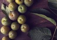 Dall'alto di prugne mature fresche e foglie verdi messe su tavolo di legno di giorno — Foto stock