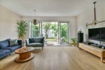 Interior design di ampio soggiorno con divano e televisore appeso sopra lettore musicale in cottage con porte a vetri aperti — Foto stock