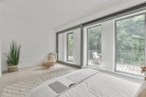 Interior del dormitorio luminoso con cama cómoda con almohadas de colores y ventana abierta a la luz del día - foto de stock