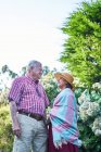 Ніжна старша пара дбайливо дивиться один на одного з ніжністю, стоячи біля квітучих чагарників на природі — стокове фото