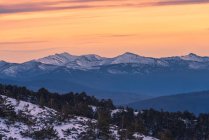 Paisagem de tirar o fôlego de encosta de colina coberta de neve e árvores contra altas montanhas rochosas sob o céu brilhante ao nascer do sol — Fotografia de Stock