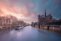Bateau touristique flottant sur les eaux ondulantes de la Seine devant la cathédrale catholique médiévale Notre Dame de Paris au coucher du soleil — Photo de stock