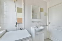 Interior do banheiro espaçoso com paredes de azulejos brancos e espelho sobre pia de cerâmica projetado em estilo mínimo — Fotografia de Stock