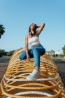 Fröhliche junge Afroamerikanerin in trendiger Kleidung hockt auf symmetrischer Konstruktion und schaut in der Stadt weg — Stockfoto