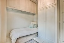 Комфортабельная кровать с одеялом в минималистском стиле в спальне с белым столом и шкафами в современной квартире — стоковое фото