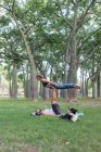 Full length of concentrate couple in activewear doing asana while practicing acroyoga together in green park in daylight and with their dog lying down to watch them — Stock Photo