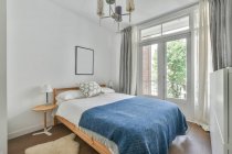 Interior do quarto elegante com cama confortável perto da janela e paredes claras durante o dia — Fotografia de Stock