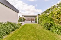 Зелений трав'янистий газон і тропічні рослини на подвір'ї сучасного будинку з затишною лаунж-зоною зі зручними диванами в сонячний день — стокове фото