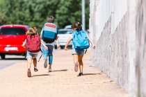 Анонимные школьники с рюкзаками, бегущими по мощеной дорожке в солнечном городе на размытом фоне — стоковое фото