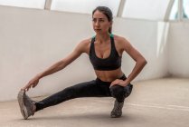 Giovane sportiva etnica flessibile in abbigliamento attivo stretching gamba durante l'allenamento durante il giorno — Foto stock