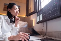 Side view of concentrated Asian female working on computer with charts showing dynamic of changes in value of cryptocurrency at convenient workplace — Stock Photo