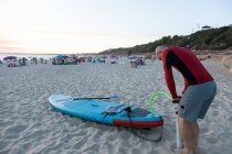 Вид сбоку серфера-мужчины в гидрокостюме и доске SUP, стоящего на берегу моря и готовящегося к серфингу — стоковое фото