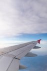 Through aircraft window view of fluffy clouds above sea and terrain during trip in daytime — Stock Photo