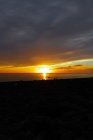 Сценічний вид туристичних силуетів, що милуються безконечним океаном від берега під хмарним небом з сяючим сонцем у сутінках. — Stock Photo