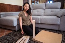 Молодая внимательная этническая женщина монтажный стол на декоративном ковре против дивана в светлом доме комнате — стоковое фото