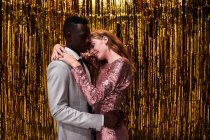 Vue latérale du jeune couple romantique multiracial dans des vêtements élégants embrassant tout en célébrant le réveillon du Nouvel An — Photo de stock