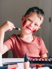 Charming child with makeup applicator looking at camera at table with eyeshadow palette — Stock Photo
