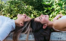 Вид збоку усміхненої жінки-підлітка з акне лежить на тлі кращого друга з закритими очима на лавці в парку — стокове фото