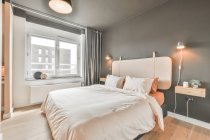 Cómoda cama con ropa de cama ligera colocada en un elegante dormitorio durante el día - foto de stock